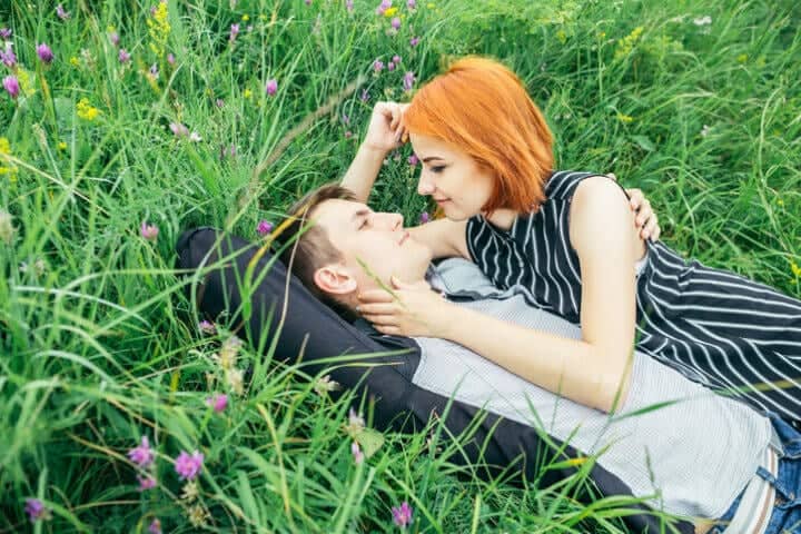 Young happy beautiful couple man and woman lying outdoors on the bright sunny day on green lawn and looking each other