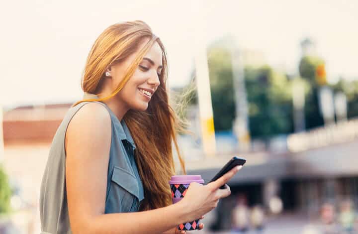 Woman using a smart phone and drinking coffee outdoor in the city.