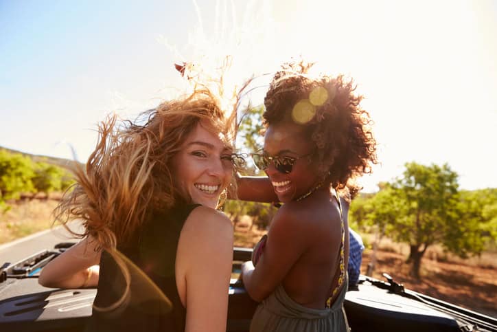 Two women standing in the back of open car turning to camera
