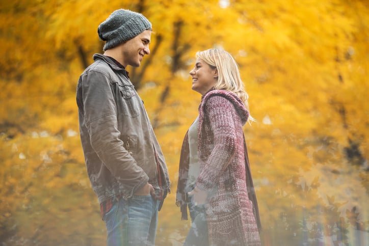 Young happy couple in autumn park talking to each other. The view is through the glass.