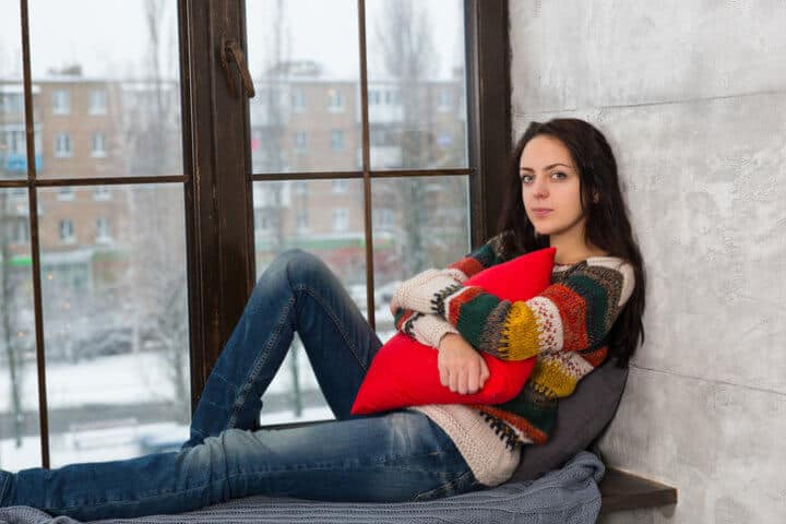 Young woman lying down on the windowsill hugging a pillow and looking at the camera