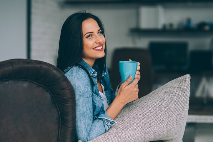 Woman drinking coffee and sitting on an armchair at home.