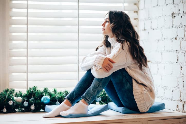 Young beautiful woman relaxing on window sill in christmas decorated home.