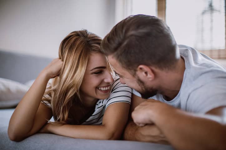 Happy Young Couple Flirting Under Bed Sheets In the Early Morning.