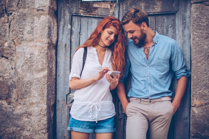 Young tourist couple, exploring foreign city. Standing by old doors and checking digital map. Wearing casual clothes and backpacks.
