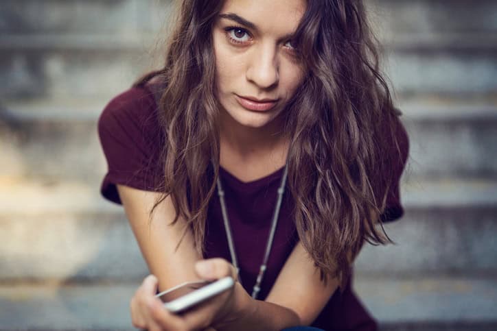 Brown haired girl looking at camera and holding her mobile phone