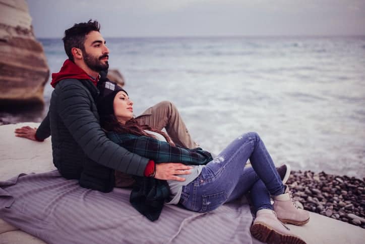 Romantic couple date sitting on a rock at the beach