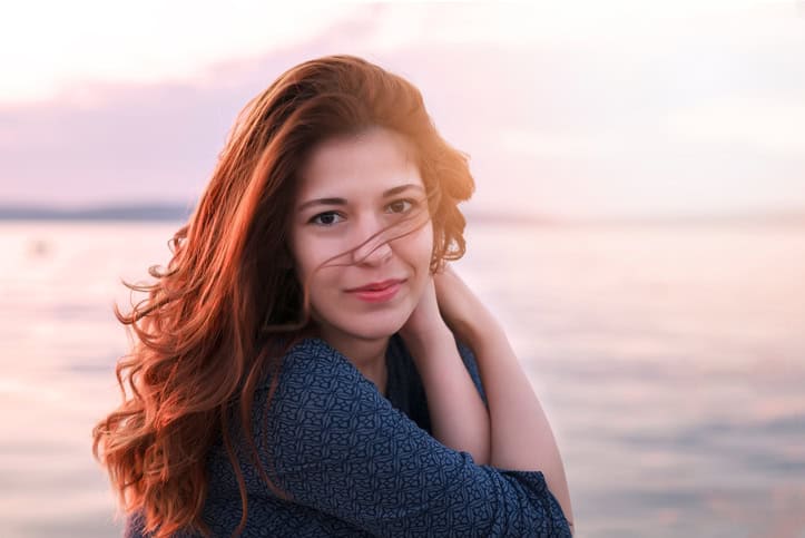Happy young woman at seaside sitting on a dock during sunset