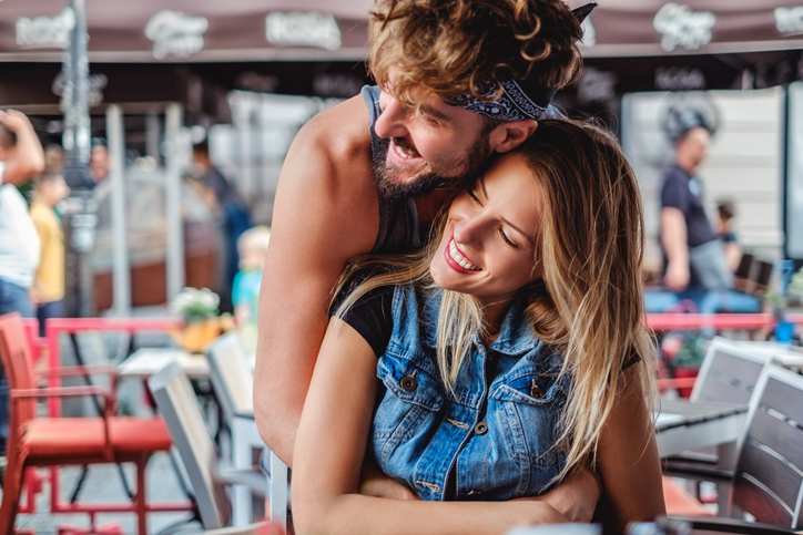 Boyfriend hugging girlfriend in a coffee shop and they are smiling
