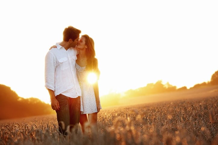 An affectionate young couple walking through a field holding each other