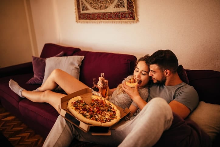 Couple eating pizza together on the couch.
