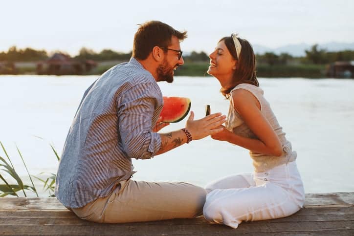 Young couple eating watermelon by the river during the sunset
