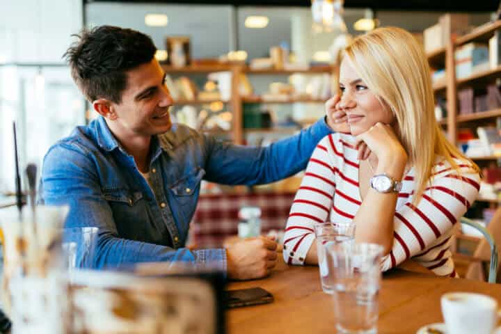 A couple sitting together in a abr, the man is complimenting the woman and touching her hair