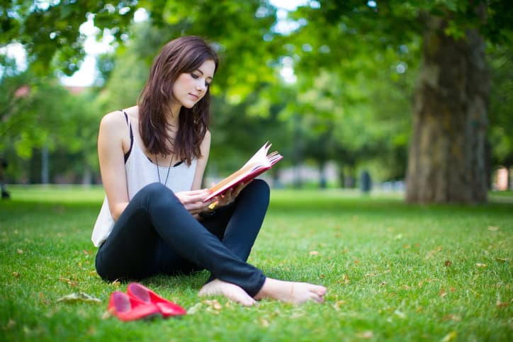 Attractive young woman sitting on the green grass with a book.