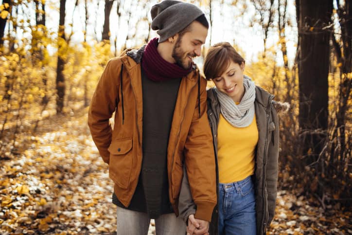 Couple happily walking through sunny forest in autumn