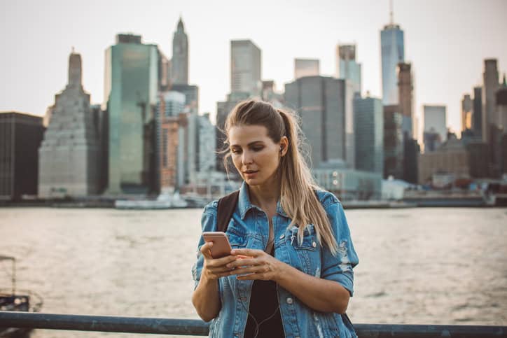 Woman in New York using smart phone in front of skyline at dusk