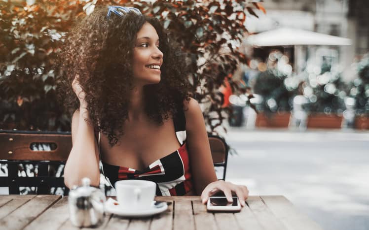 Curly laughing woman in a street cafe with the cellphone