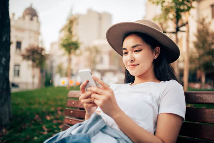smiling woman texting on park bench