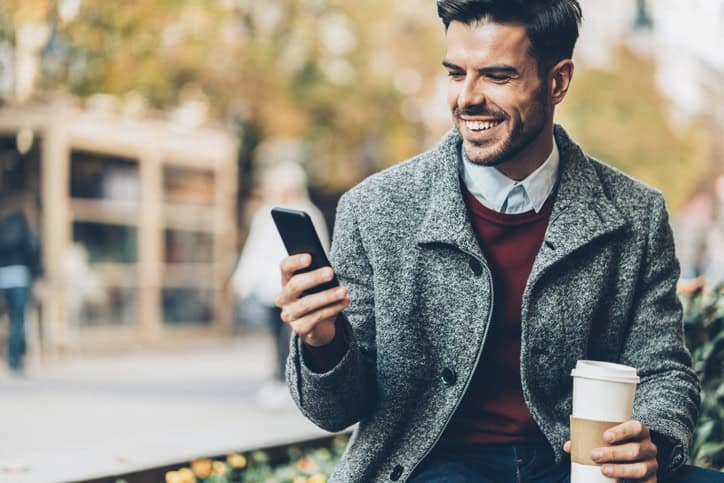 Young businessman texting and drinking coffee in the city