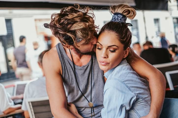 Boyfriend kissing angry girlfriend in a cafe and she is not looking at him.