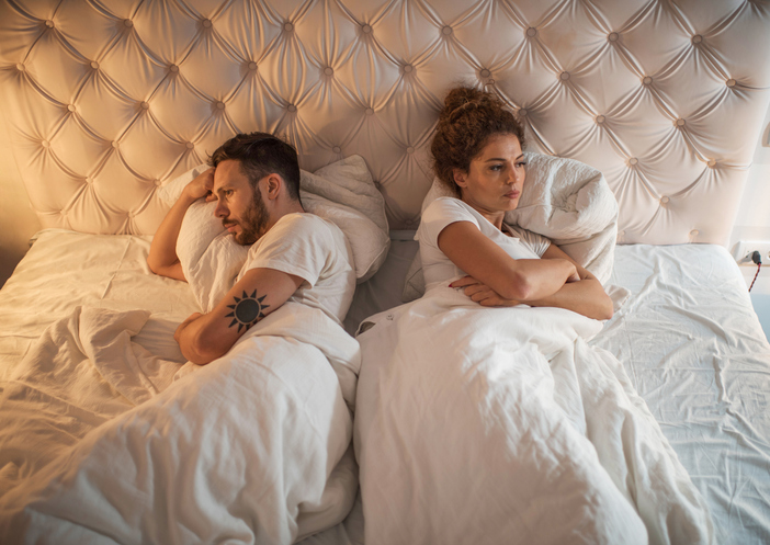 Above view of young couple lying back to back in bed while being angry at each other.