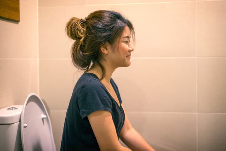 Young woman sitting on the toilet.