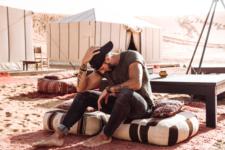 fashion man sitting on the desert in front of a tent