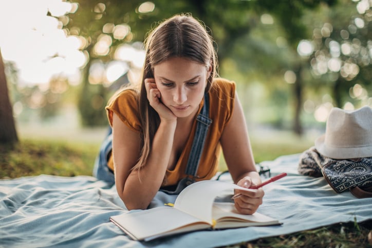 An young introverted lady lying on a blanket alone and reading 