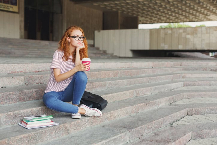 Thoughtful student girl sitting with coffee cup outdoors