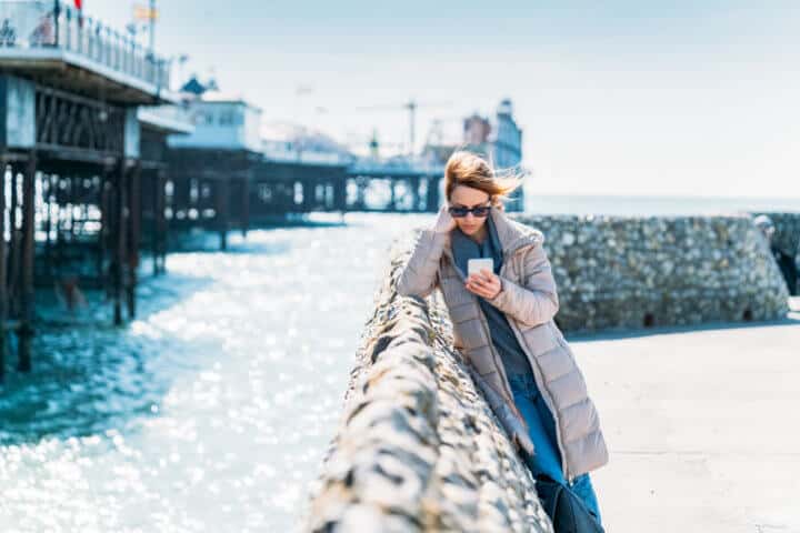 Depressed woman near the ocean text messaging