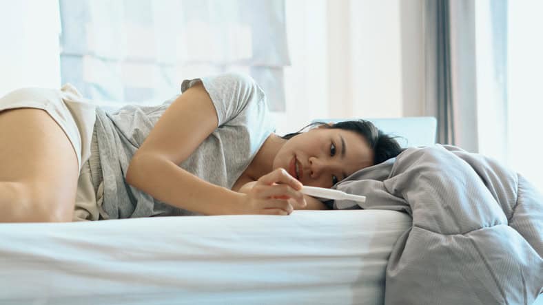 Woman in bed reading a pregnancy test.