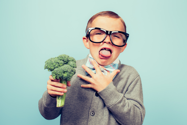 Young boy holding a head of broccoli pretending to hate it.