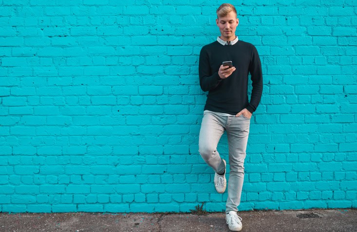Young man standing against wall and checking phone