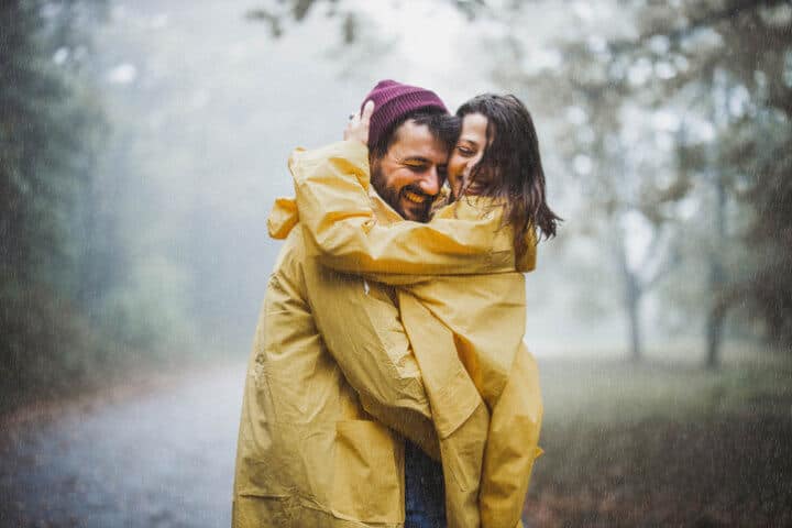 Couple embracing each other, smiling in the rain wearing raincoats