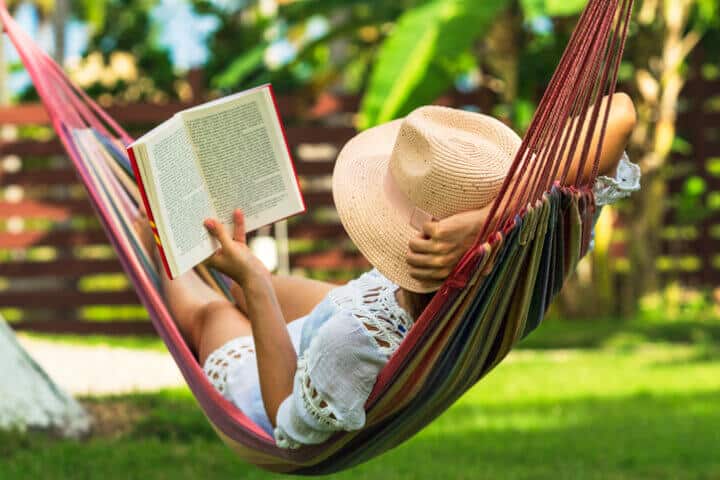 Woman reading a book in a hammock in tropical garden.