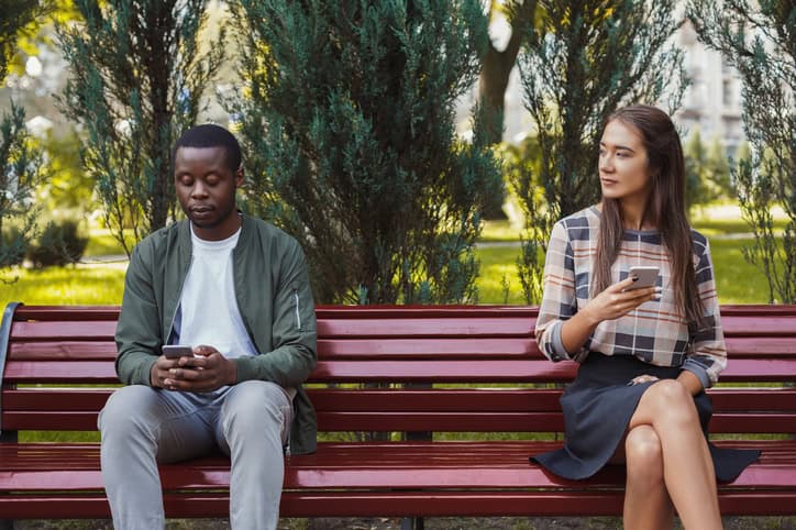mixed race copule sitting on a bench texting