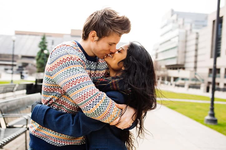 man in colorful sweater kissing woman in the street