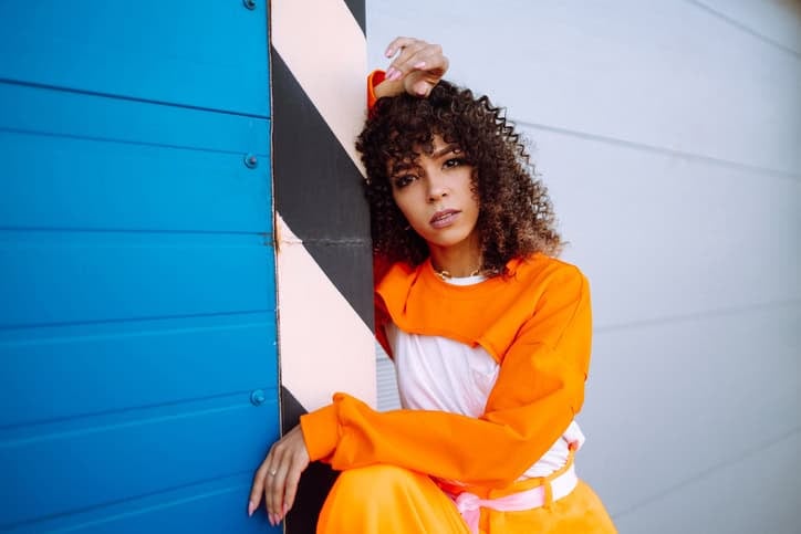 black woman in orange against wall