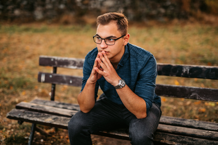 Nervous young man sitting on bench in park.