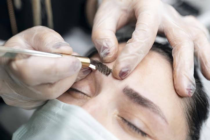 Beautician painting new eyebrows on her customer.