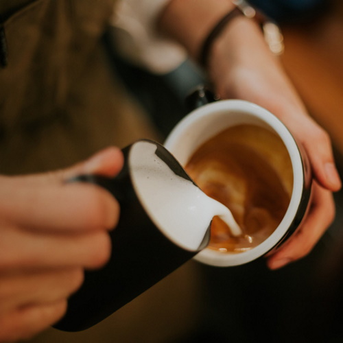Frothy milk going into a coffee cup.