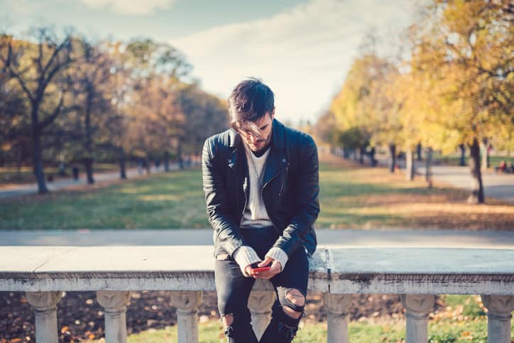 man sitting on a bridge texting