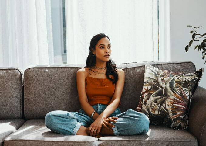 Shot of a young woman looking thoughtful while relaxing on the sofa at home