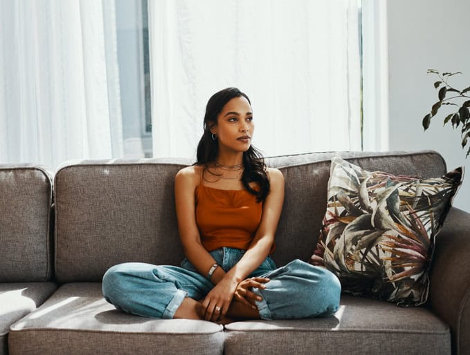 Shot of a young woman looking thoughtful while relaxing on the sofa at home