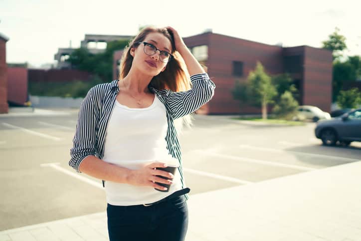Beautiful young woman dressed in stylish outfit posing for camera while strolling around city with coffee at leisure time.Pondering good looking student enjoying recreation at street with aroma drink