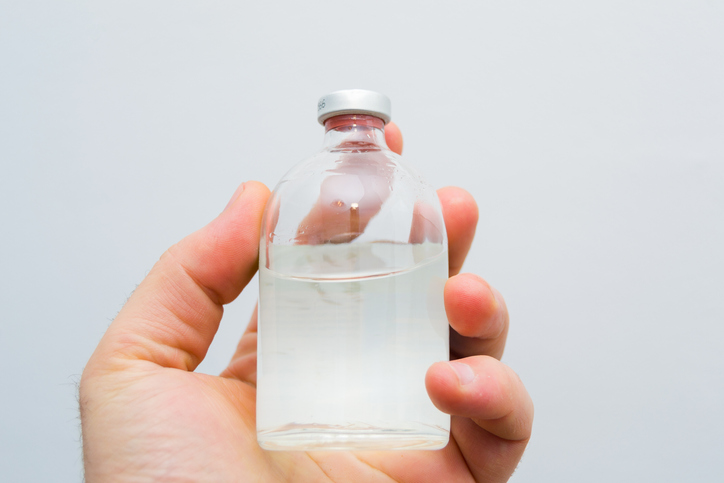 A glass bottle with transparent solution in a man's hand.