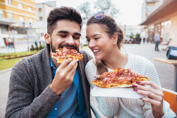 Couple eating pizza outdoors.
