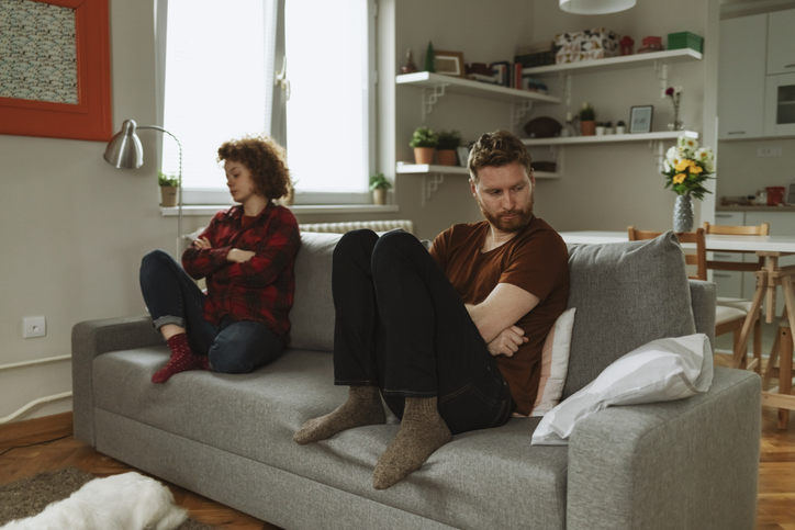 Boyfriend and girlfriend sitting on the sofa in the living room, distant from each other