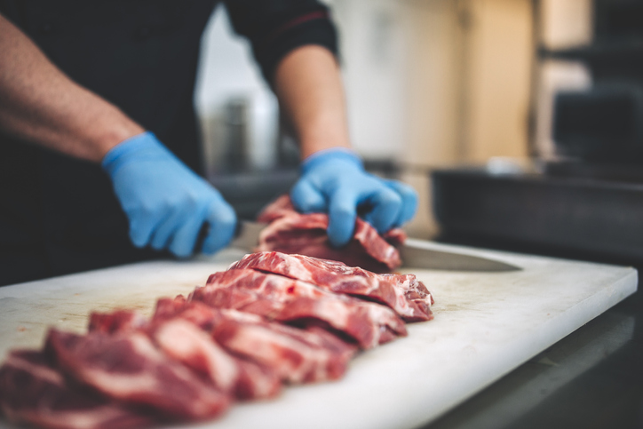 Male butcher cutting raw meat.