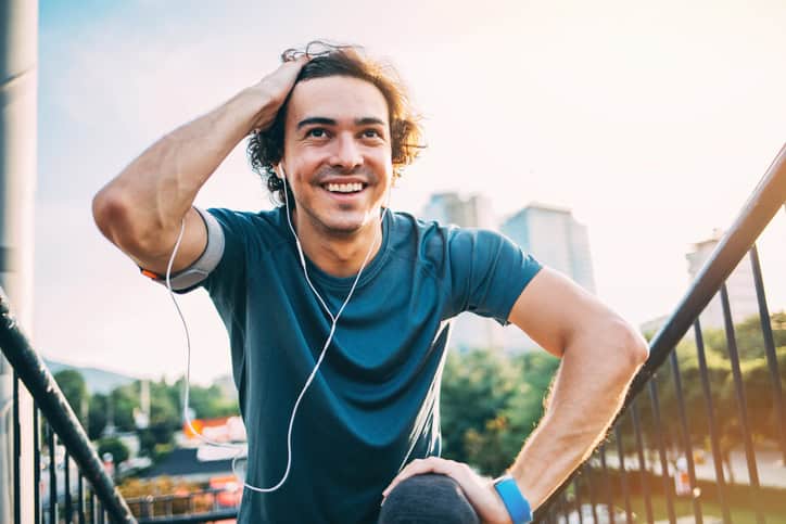 Young man in sports wear and with portable information devices making exercises at sunlight outdoors in the city